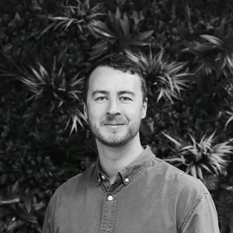 Grey scale photo of founder, Michael Shaskey in front of a leafy background. 